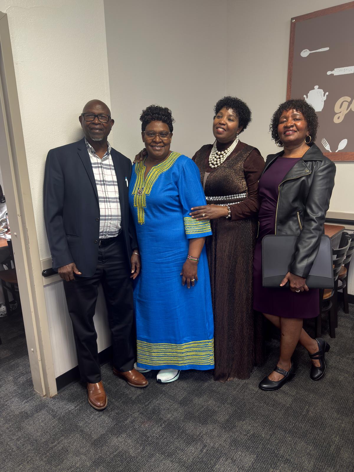Four community members posing indoors with a member wearing a blue dress
